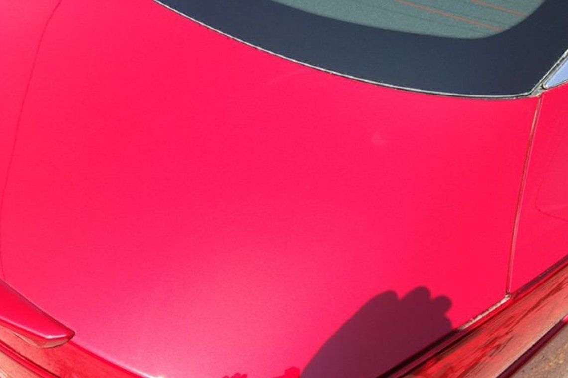 Close-up of a bright pink car hood with windshield and shadow visible