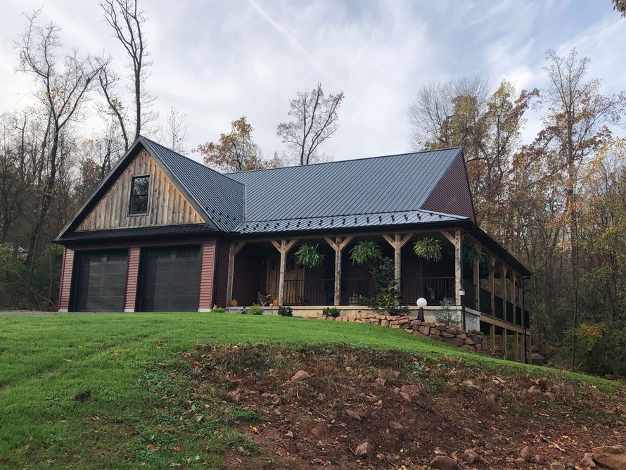 Rustic cabin with a porch and metal roof on a grassy hill beside autumn trees