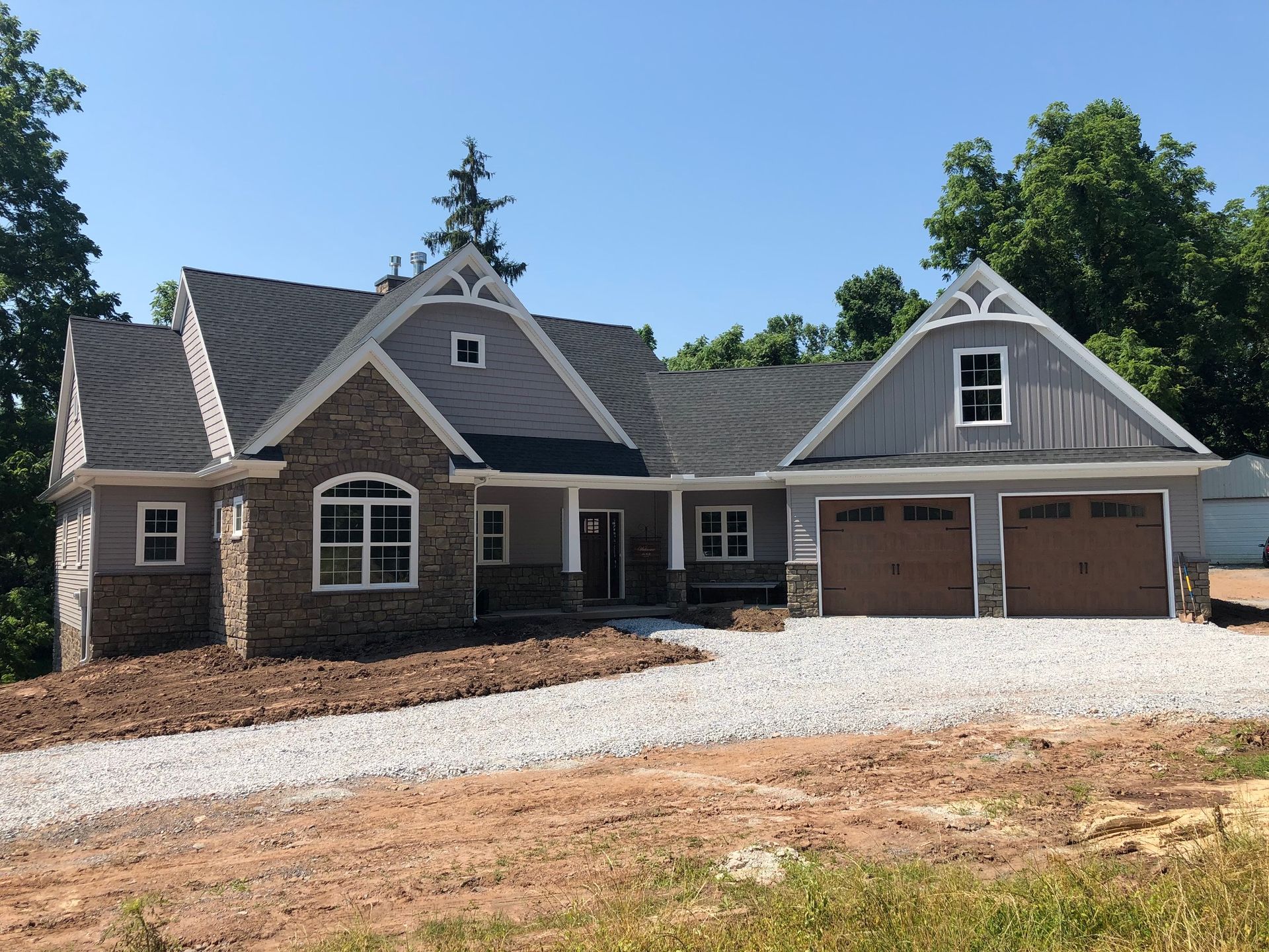 Brick house with gray gables and two-car garage on a gravel driveway under a clear blue sky