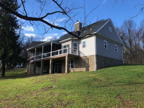 Gray two-story house with a porch on a grassy hill under a blue sky