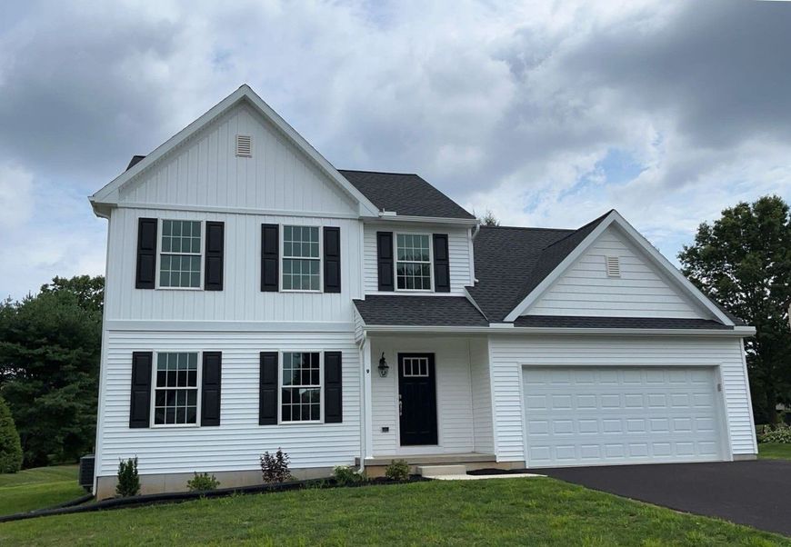 White two-story suburban house with black shutters, attached garage, and cloudy sky