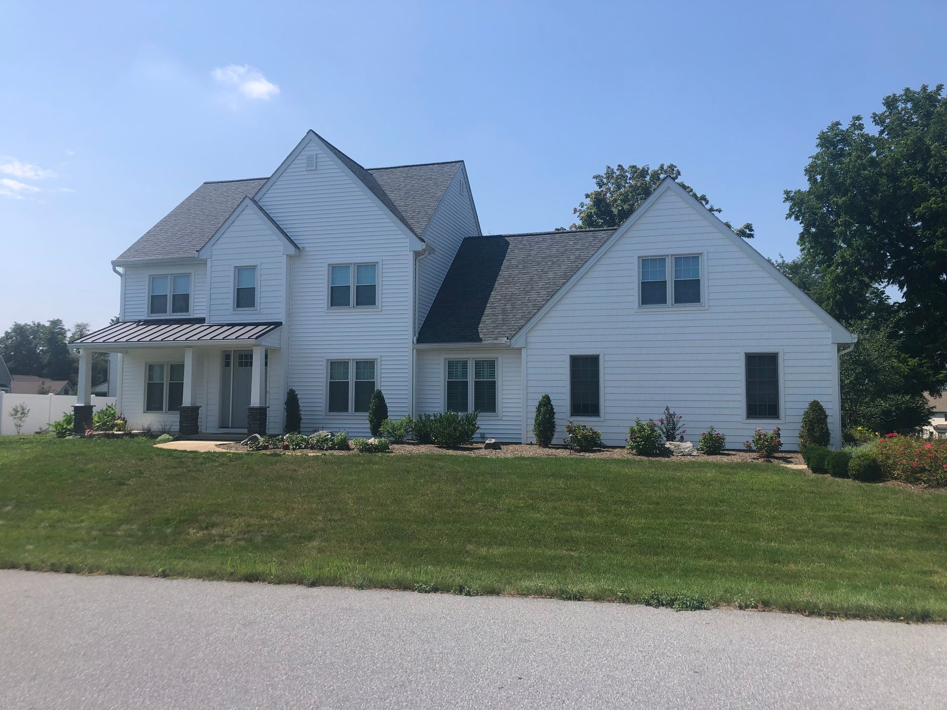White two-story suburban house with a gabled roof and front lawn on a sunny day