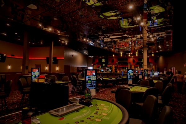 A group of people cheers while celebrating a win at a baccarat table in a brightly lit casino.