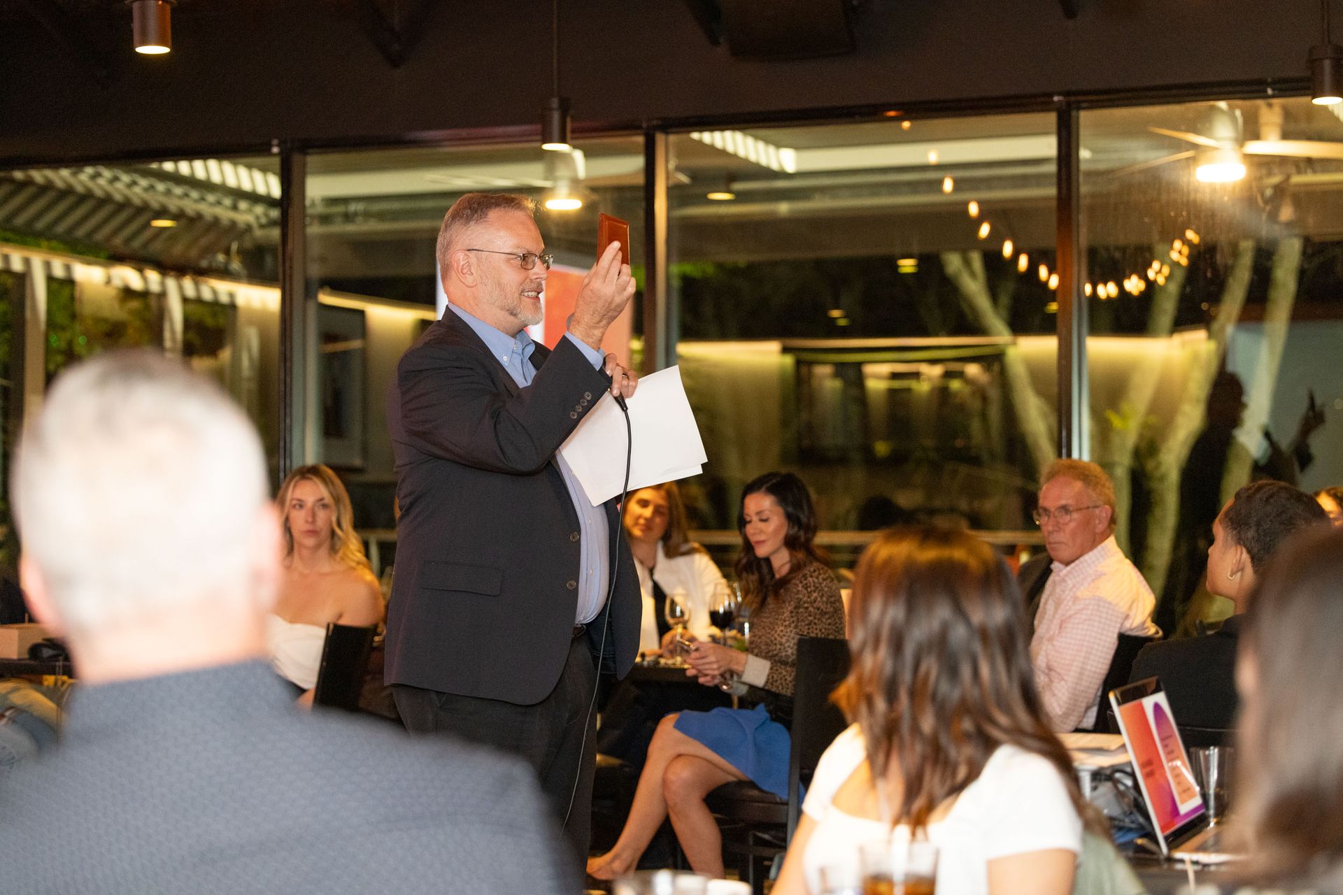 A man in a suit is giving a speech to a group of people sitting at tables.
