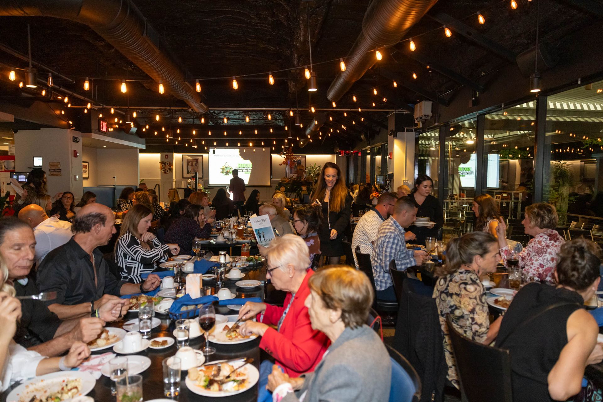 A large group of people are sitting at tables in a restaurant eating food.