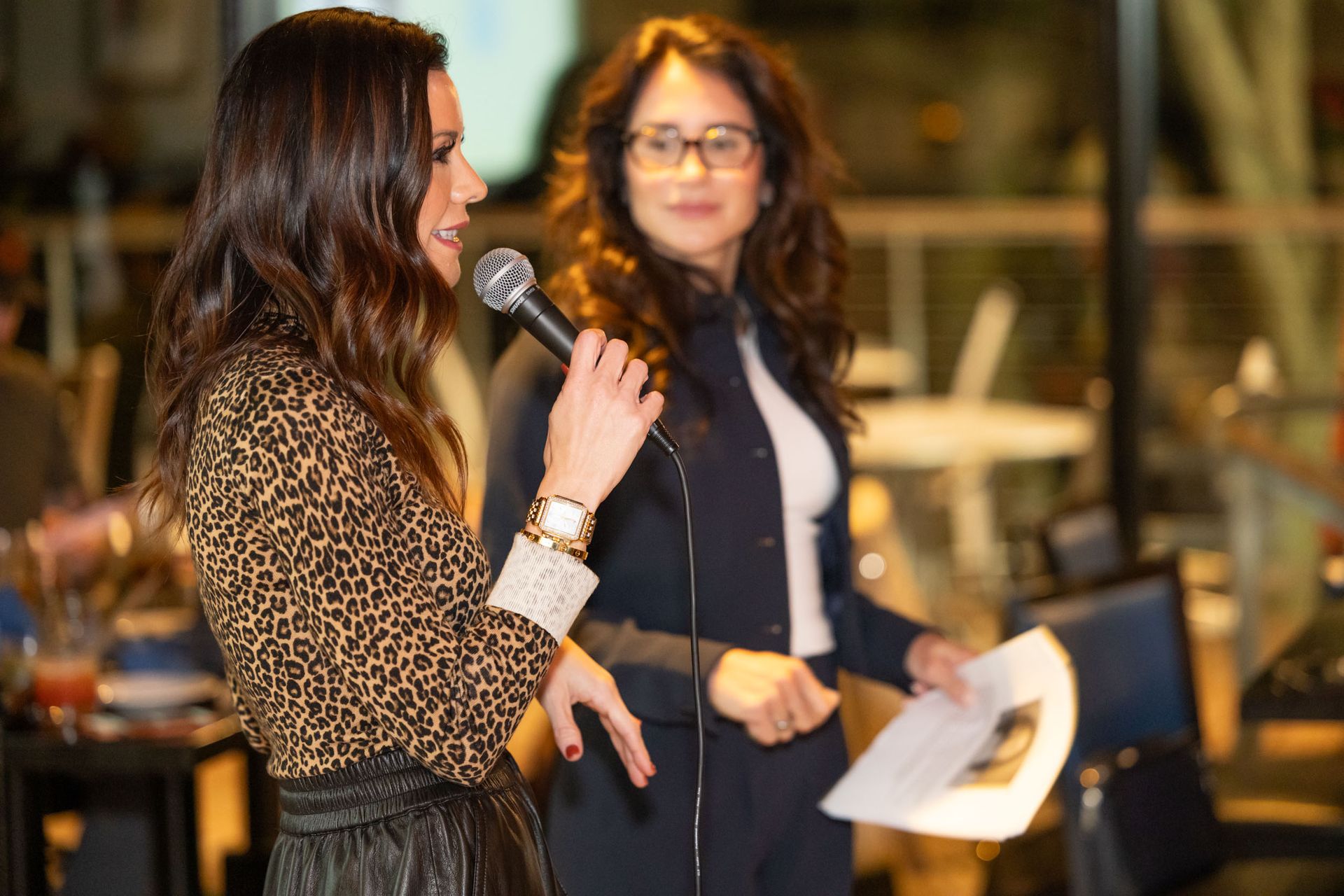 Two women are standing next to each other talking into microphones.