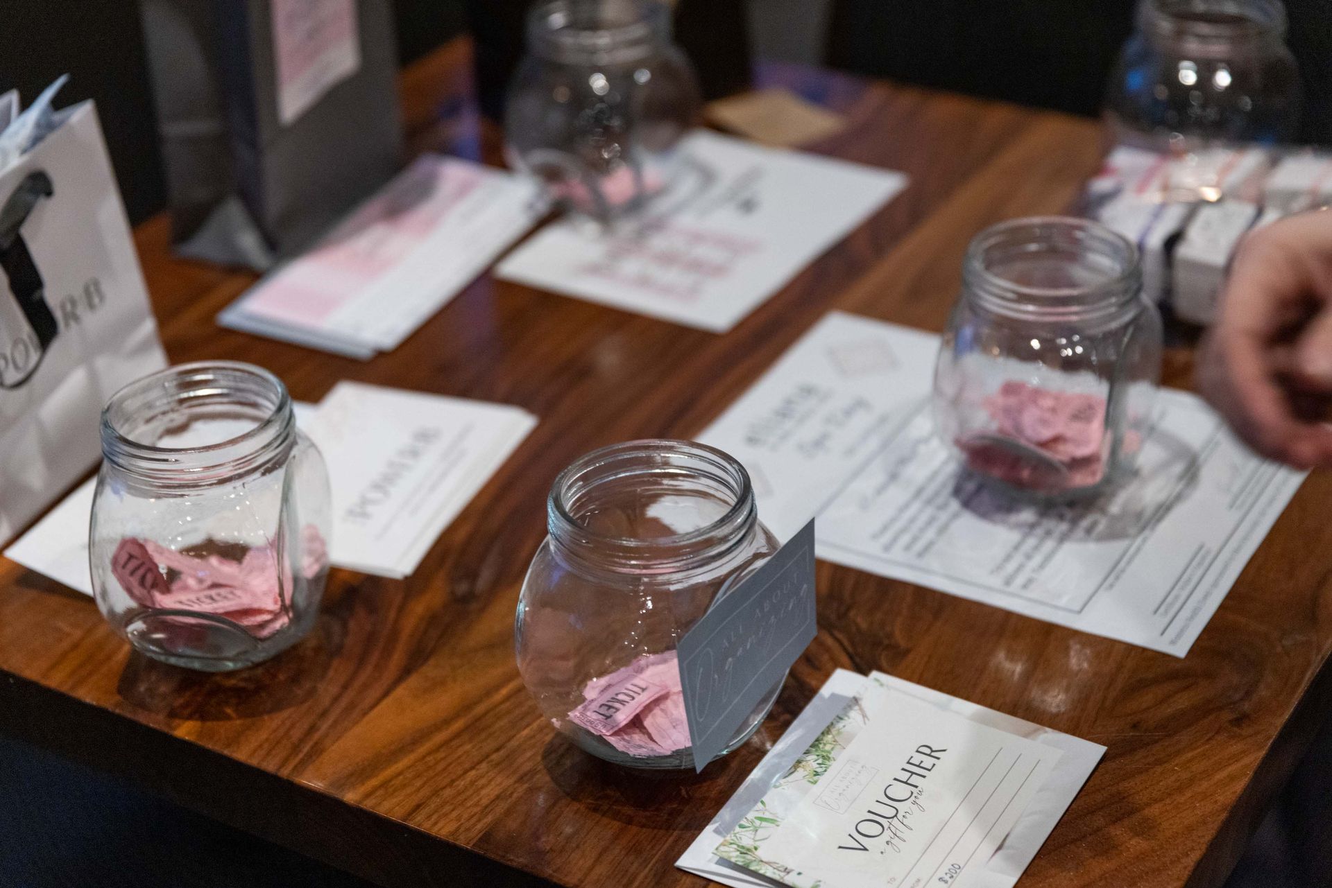 A wooden table with jars filled with pink pieces of paper on it.
