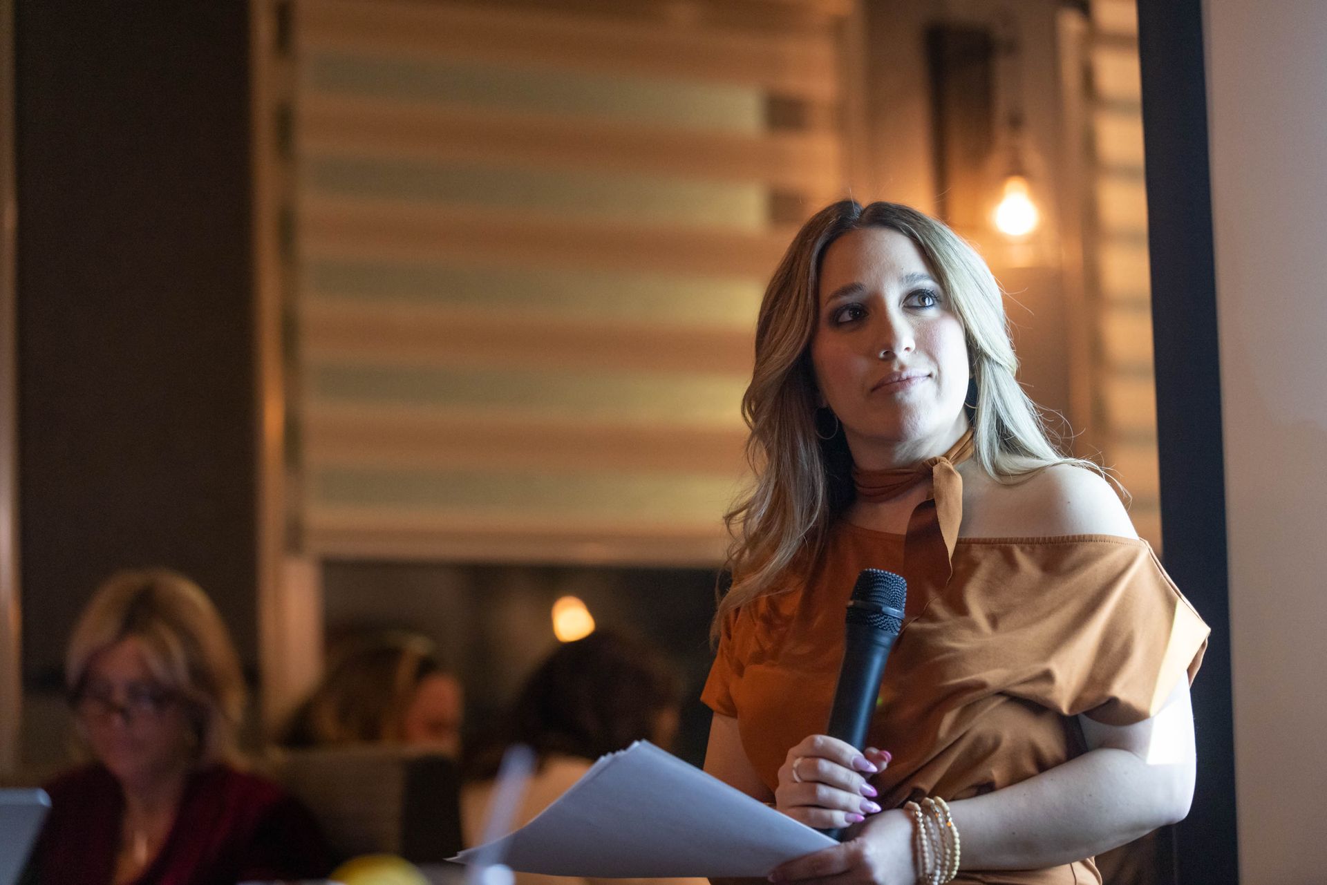 A woman is holding a microphone and a piece of paper.