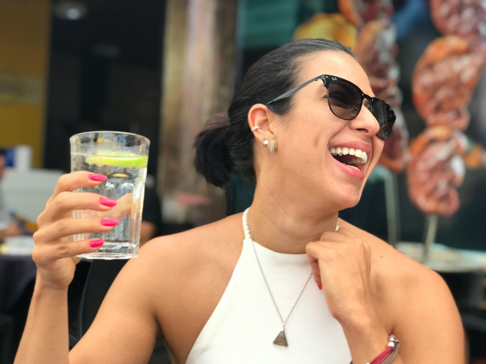 A woman wearing sunglasses is holding a glass of water and smiling.