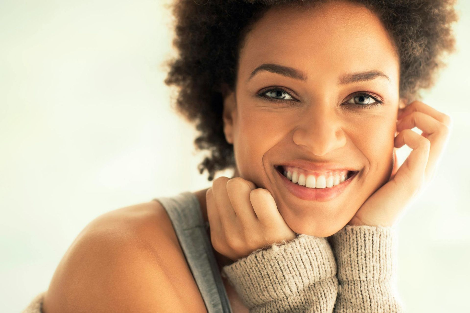 A close up of a woman smiling with her hand on her face.