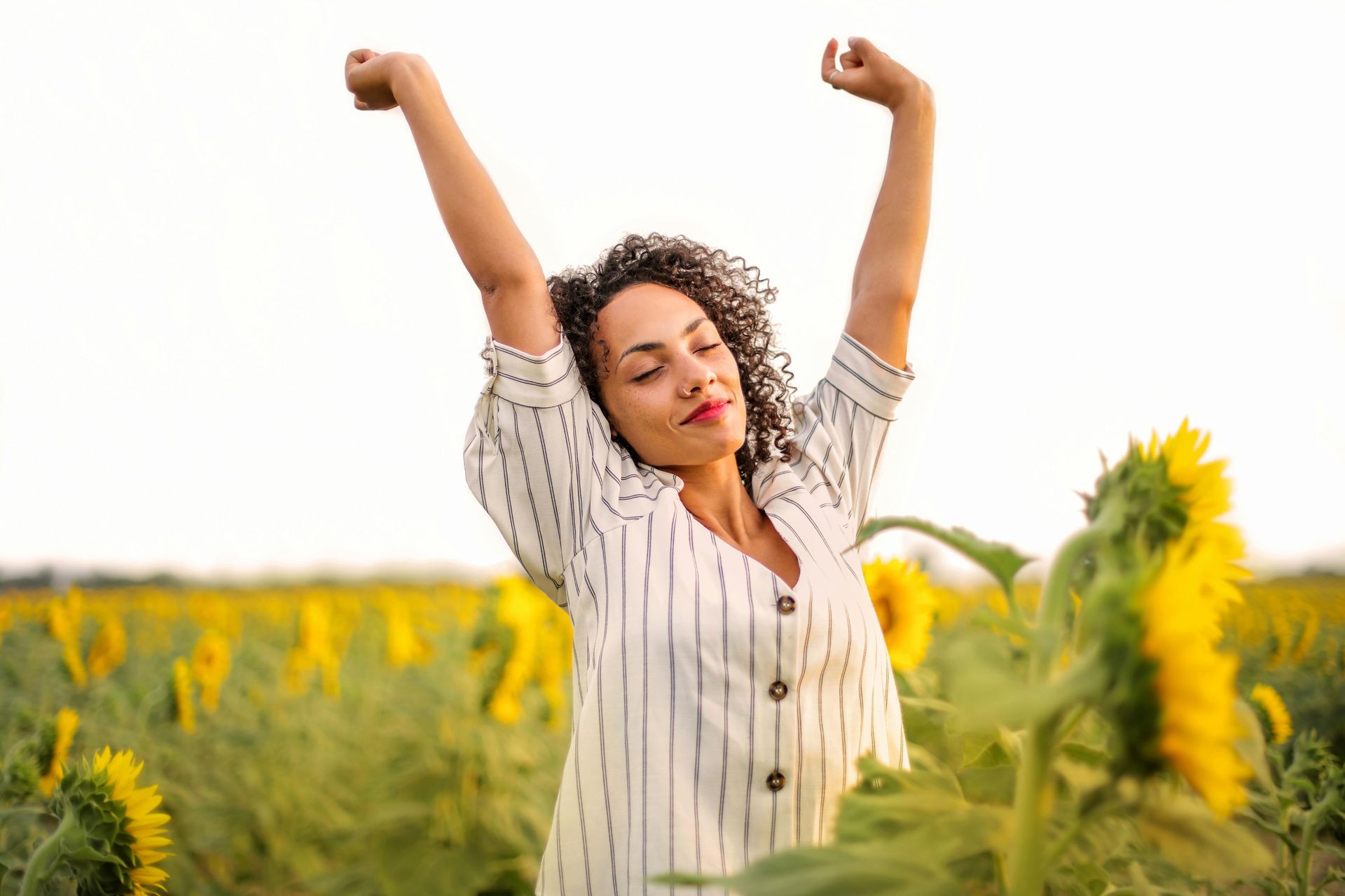 A woman is standing in a field of sunflowers with her arms outstretched.