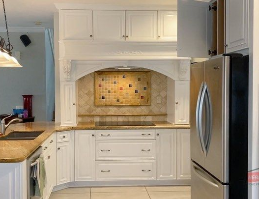 White kitchen with built-in niche, tiled backsplash, marble countertop, and stainless steel refrigerator