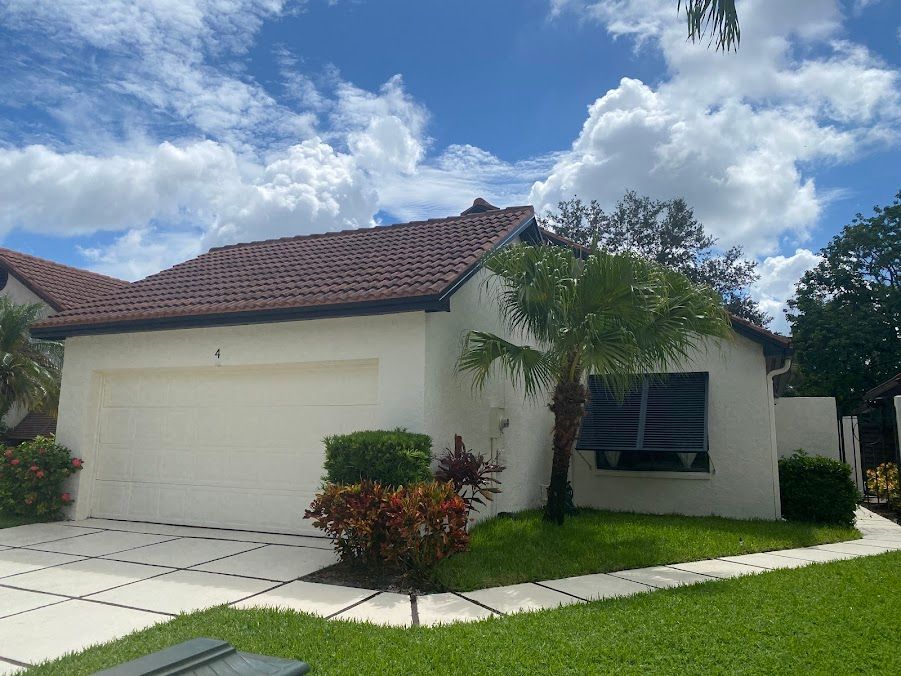 Suburban house with white garage, red tile roof, blue shutters, and manicured lawn under a cloudy sky