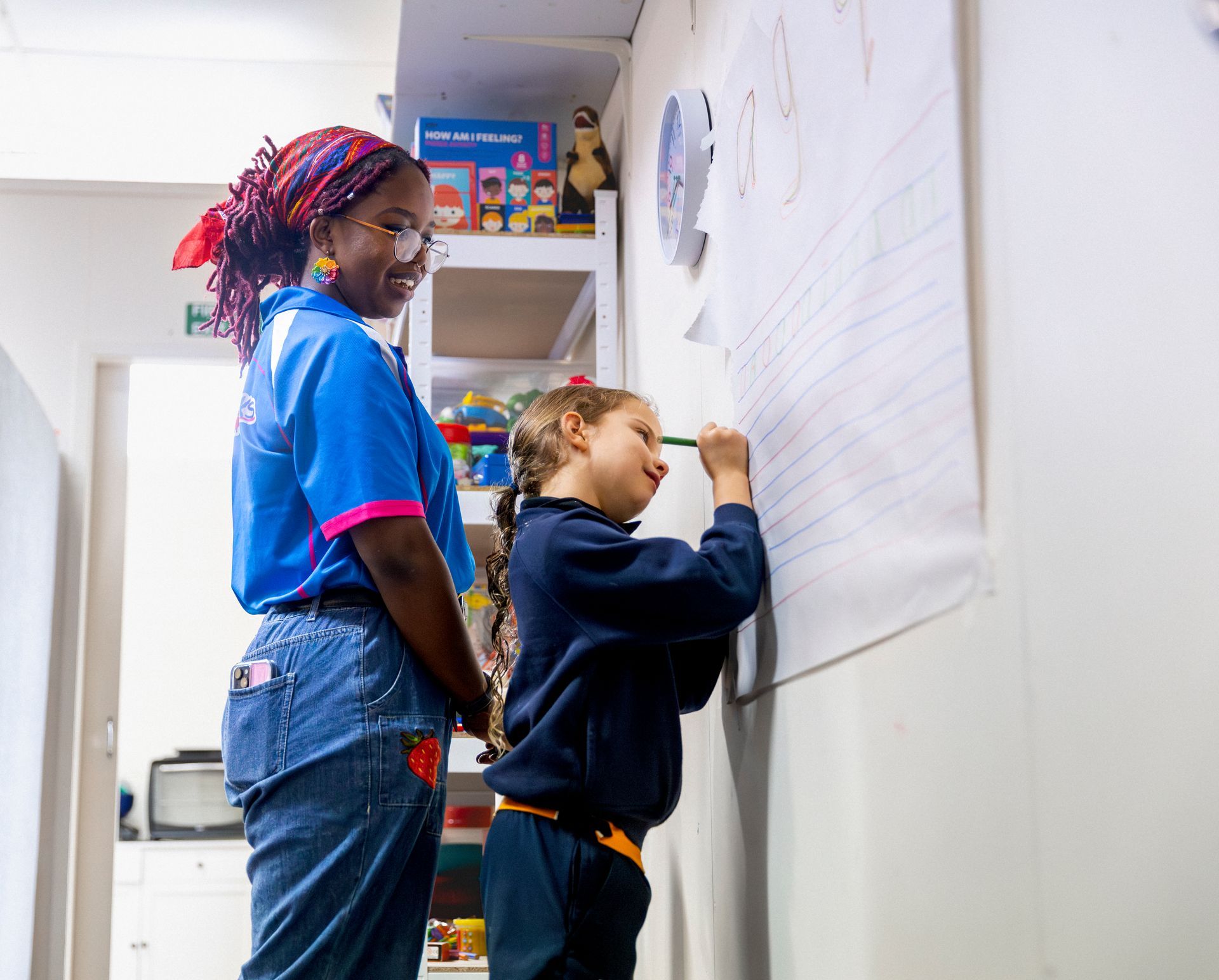 Two people writing on a large wall chart in a bright room
