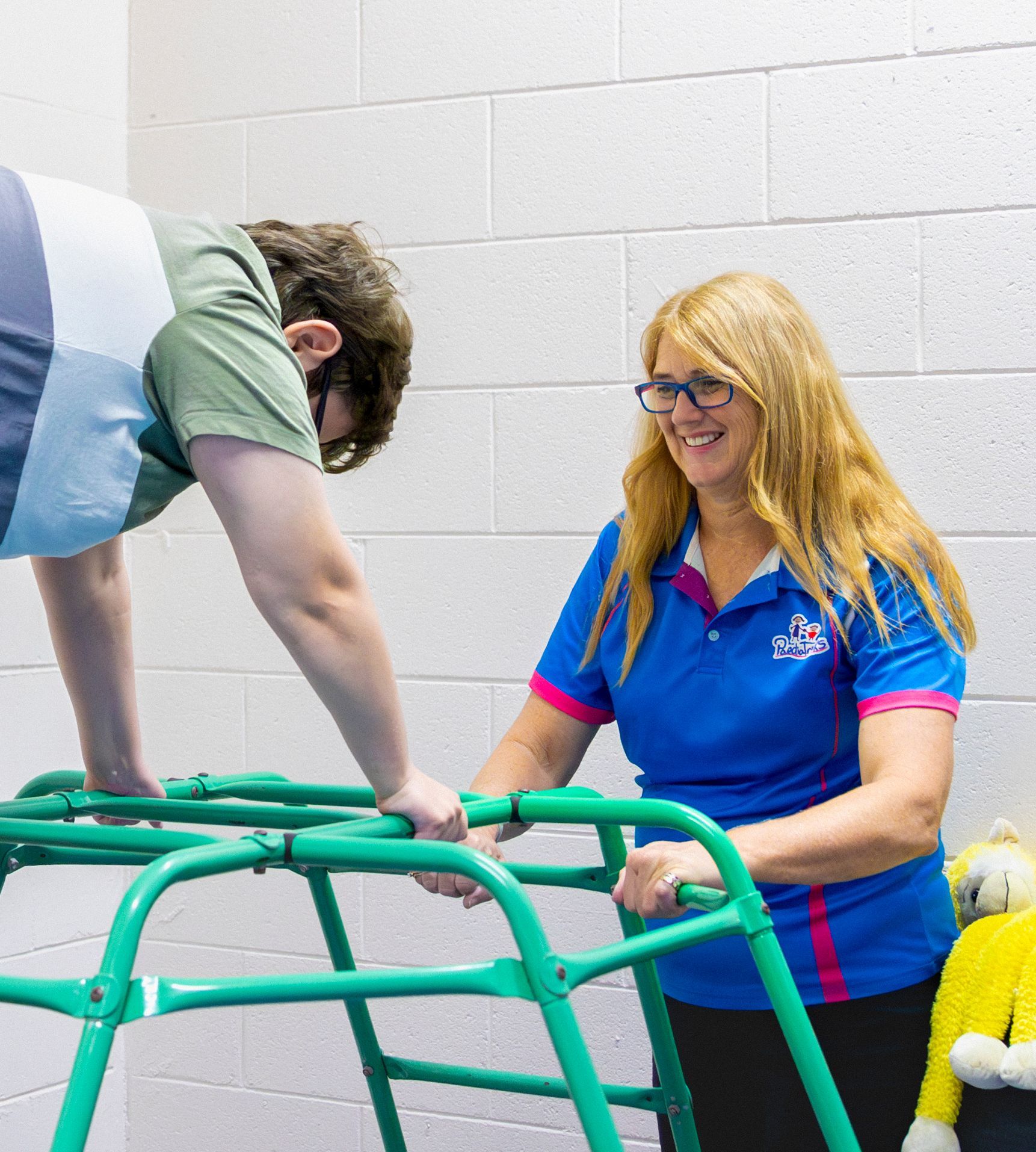 Two people smiling beside a green climbing frame in a bright indoor playroom