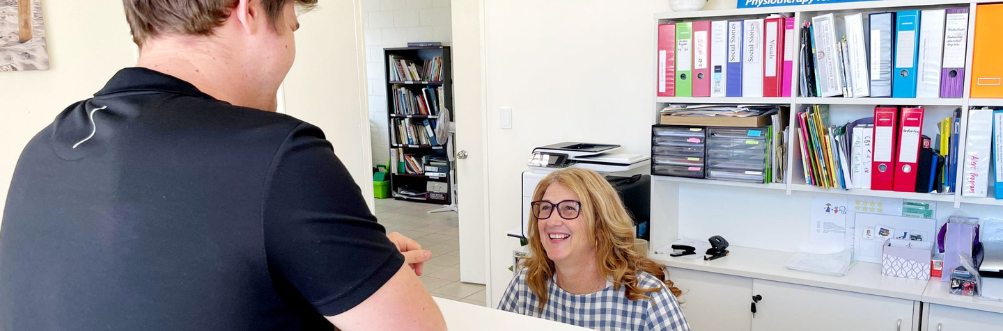 Customer speaking with receptionist at a front desk in an office with colorful binders on shelves
