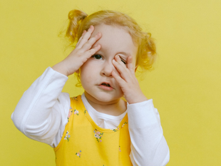 Young child in a yellow outfit rubbing their eyes against a bright yellow background