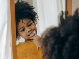 Person brushing teeth in a mirror, wearing a mustard yellow sweater.