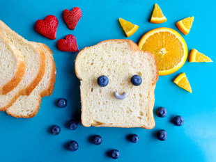 Smiling bread slice with blueberries, orange sun, strawberries, and bread slices on blue background