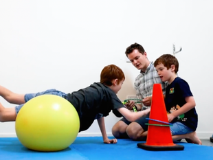 Children playing with colorful exercise balls and a cone while sitting on the floor with an adult.
