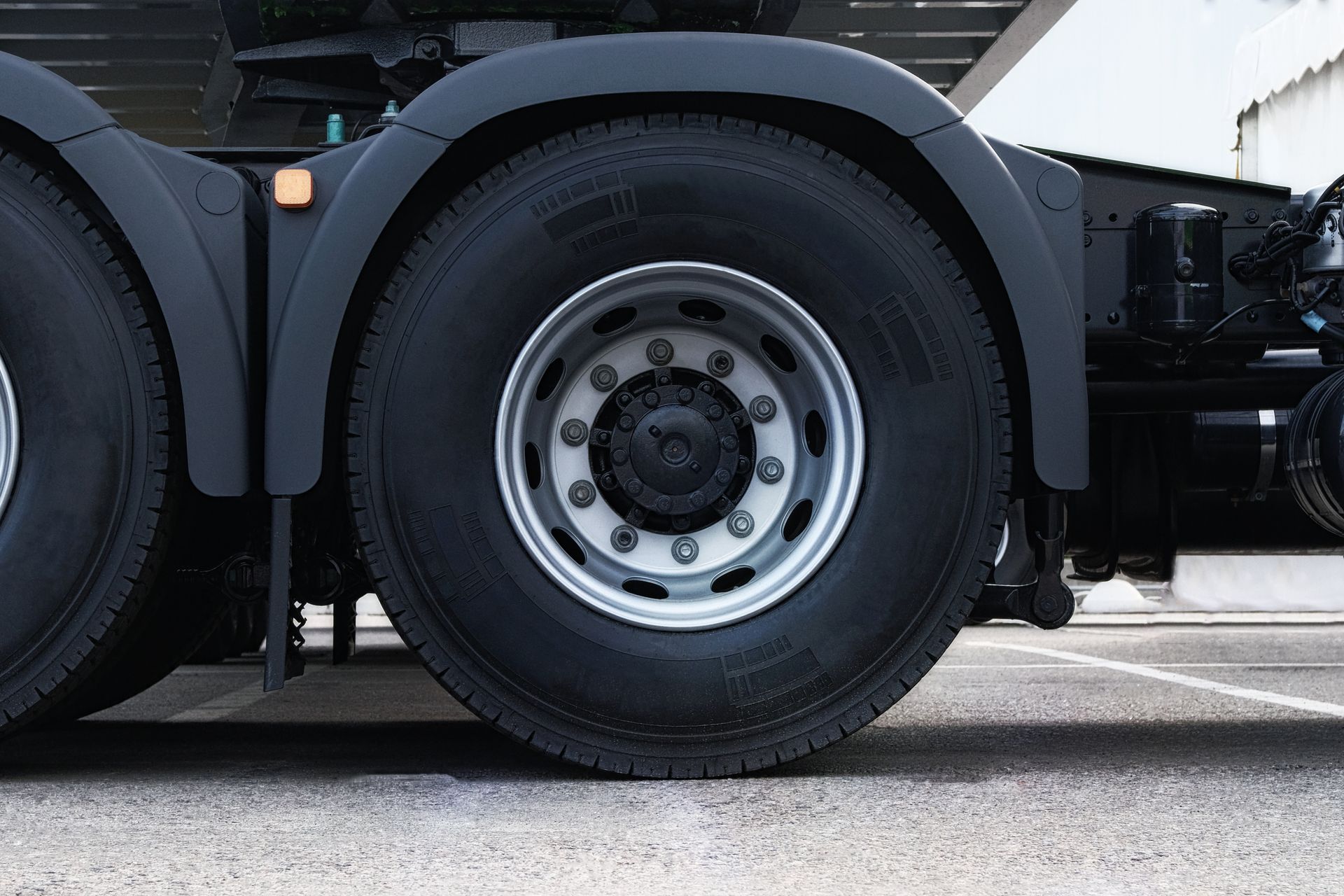 Close-up of a truck’s rear wheel and axle beside the road, with a black tire and silver rim