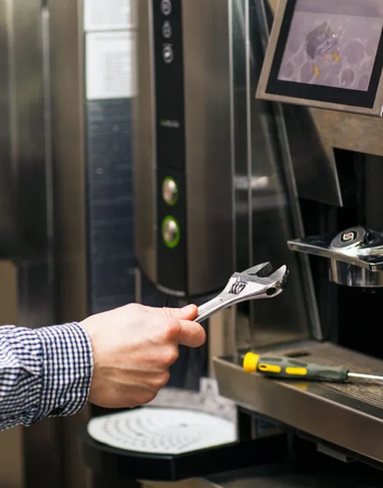 Hand using a wrench to adjust a coffee machine with a cup below