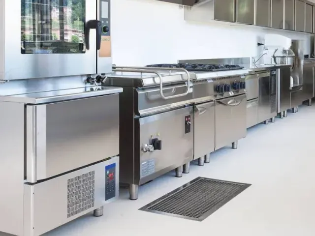 Modern commercial kitchen with stainless steel appliances and counters along a bright wall.