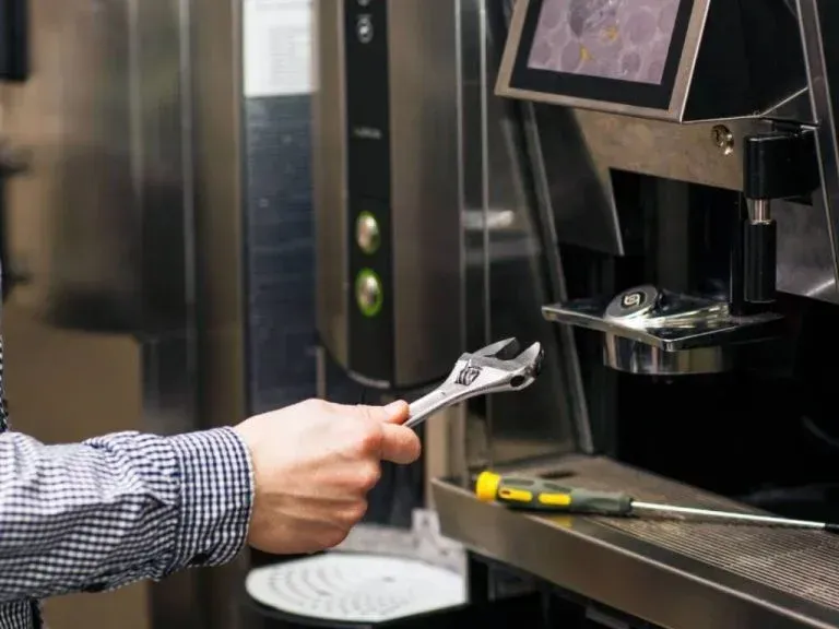 Hand holding a wrench to adjust a black coffee machine in a kitchen or break room