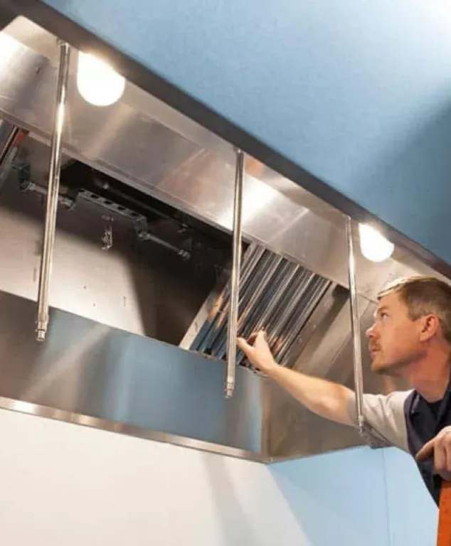 Man inspecting a stainless steel kitchen vent hood with filter panels open