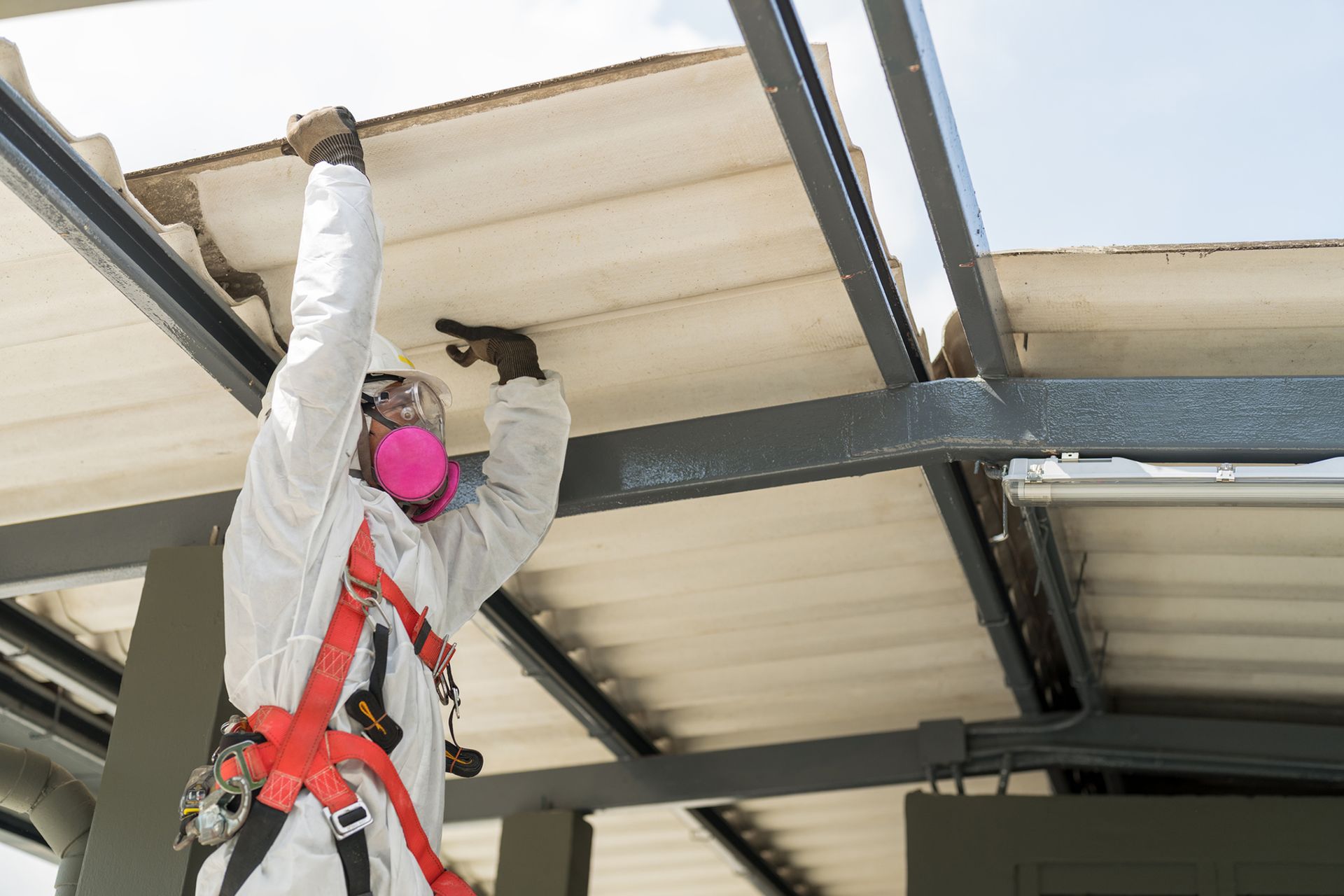 Operaio con tuta protettiva, respiratore e imbracatura, impegnato nella riparazione della struttura del soffitto all'aperto.