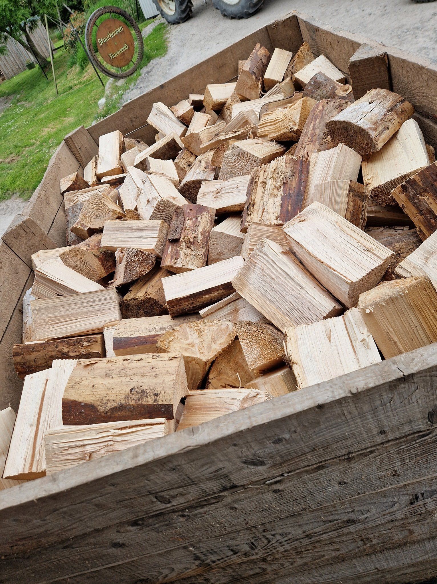 A wooden box filled with logs is sitting on the ground.