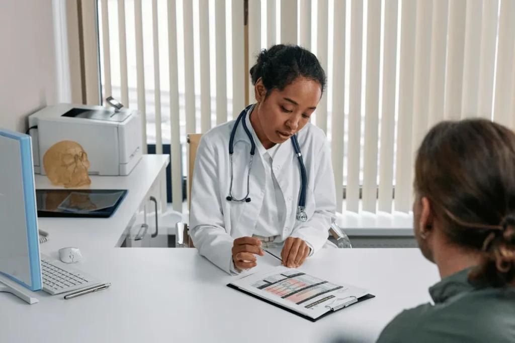 Doctor consulting a patient at a desk with medical charts in a bright clinic office