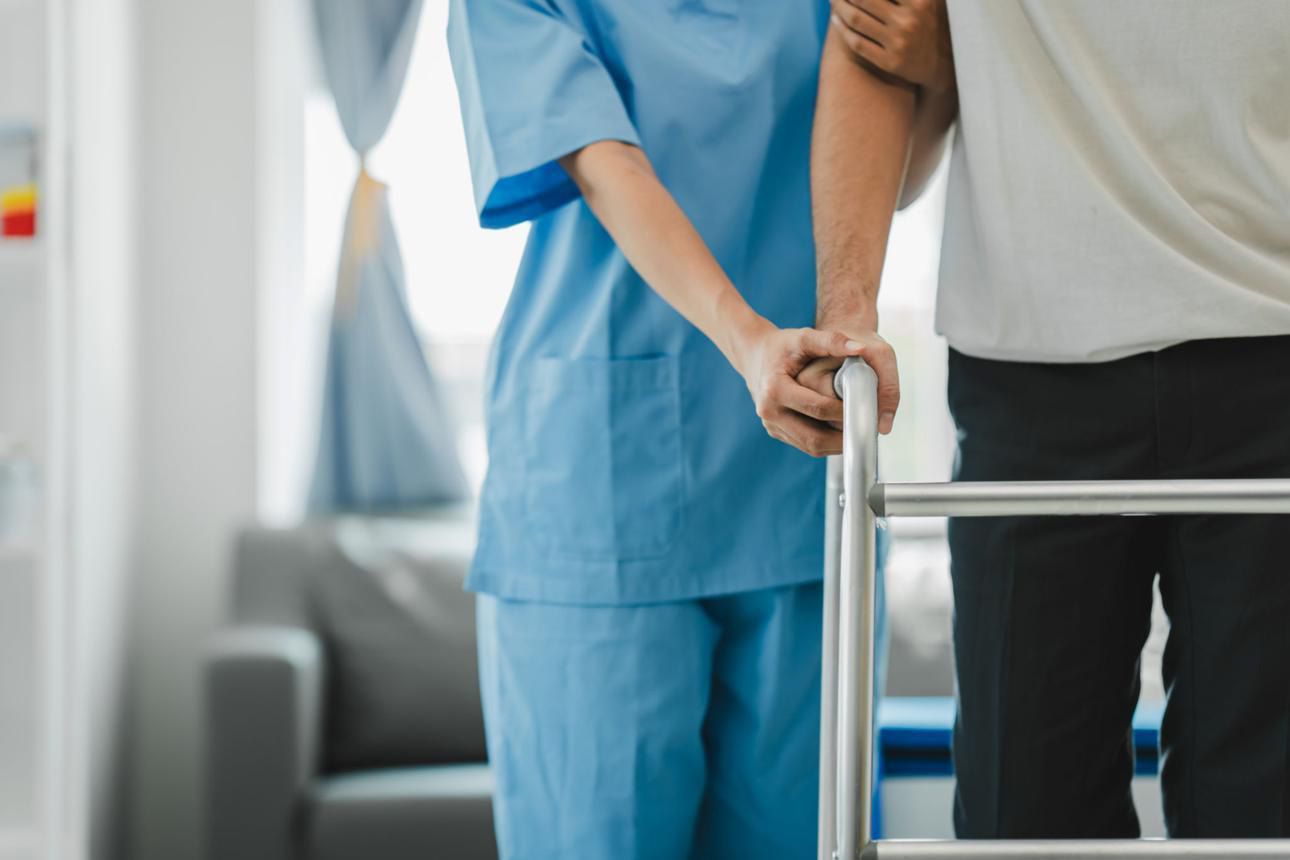 Nurse in blue scrubs helping a patient walk with a walker in a hospital room