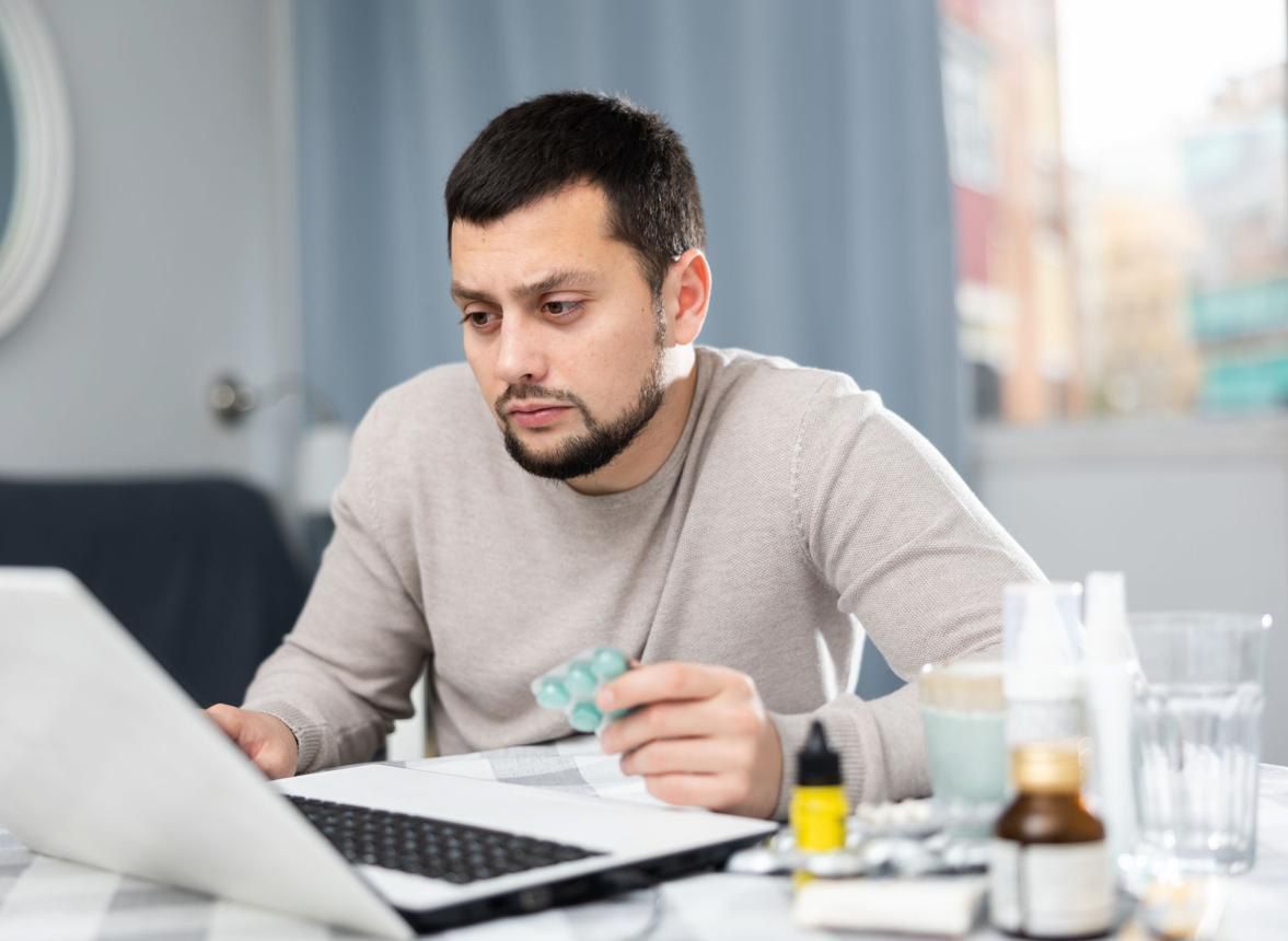 Person working at a laptop at a table, holding a small object in a bright office setting
