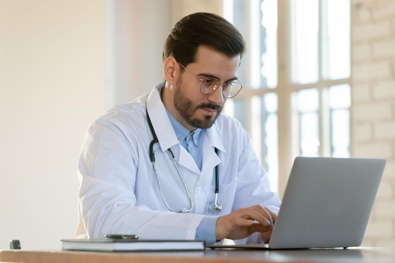 Doctor in a white coat working on a laptop in a bright office