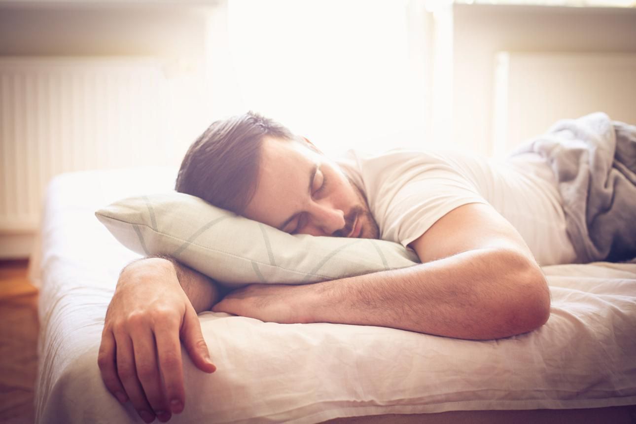 Person sleeping on a bed with a white pillow in soft sunlight