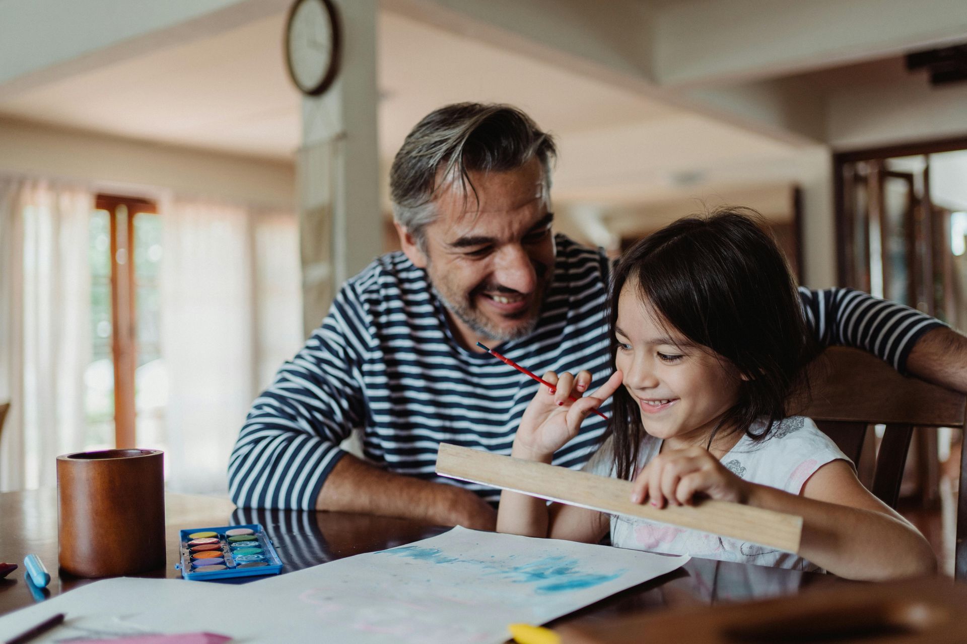 Man and child drawing together at a table. The man has an arm around the child, smiling.