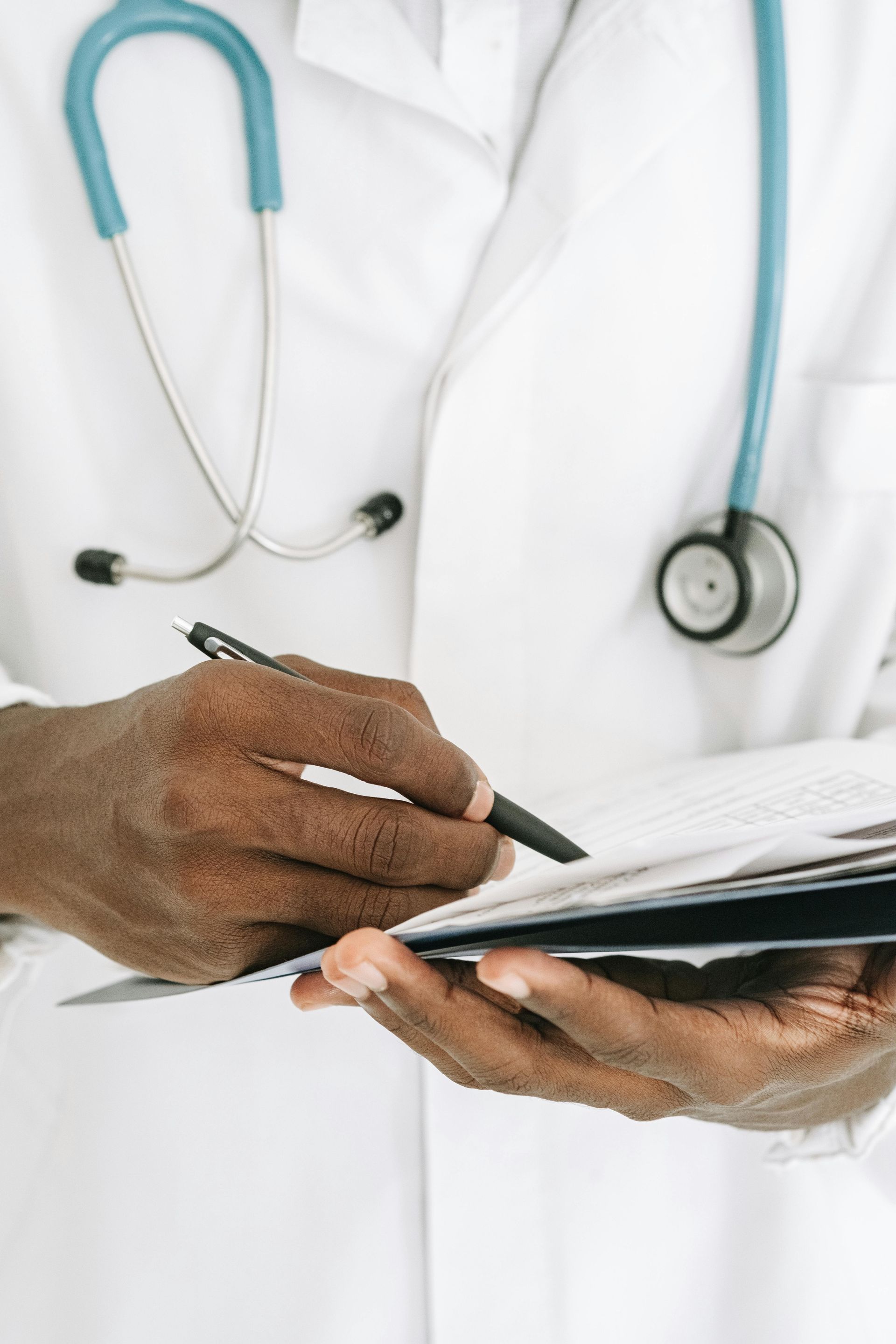 Doctor in white coat writing on paperwork, stethoscope around neck.