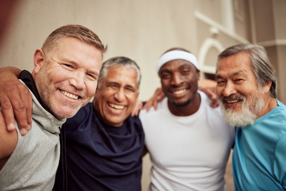 Four smiling men with arms around each other pose outdoors.