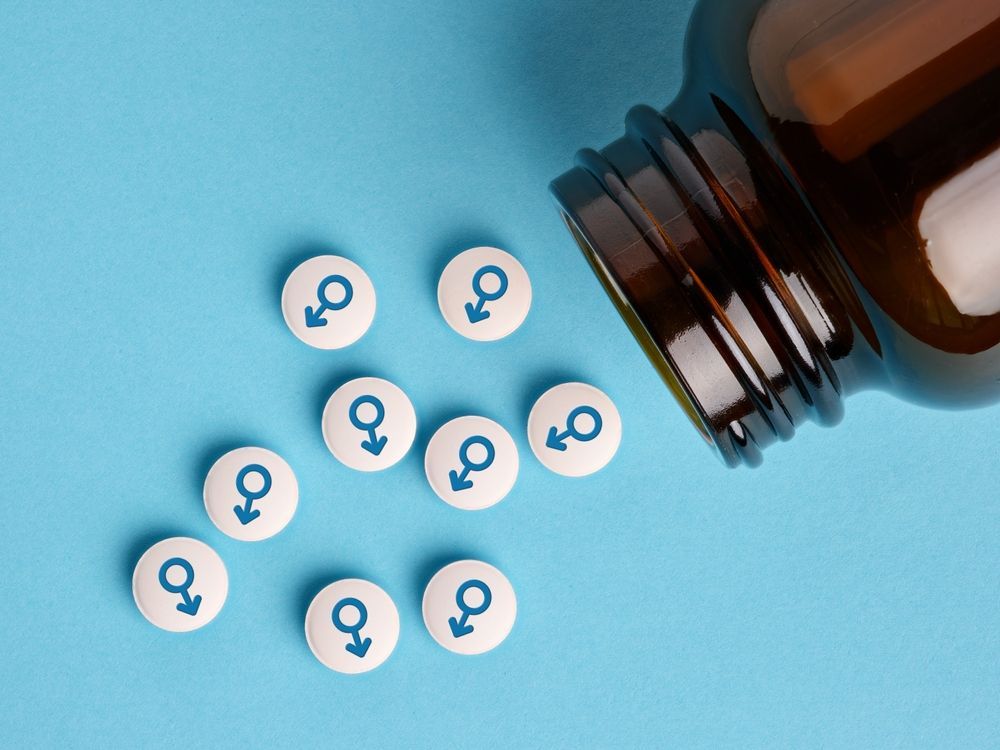 Pills with male symbol spilling from a brown bottle on a blue background.