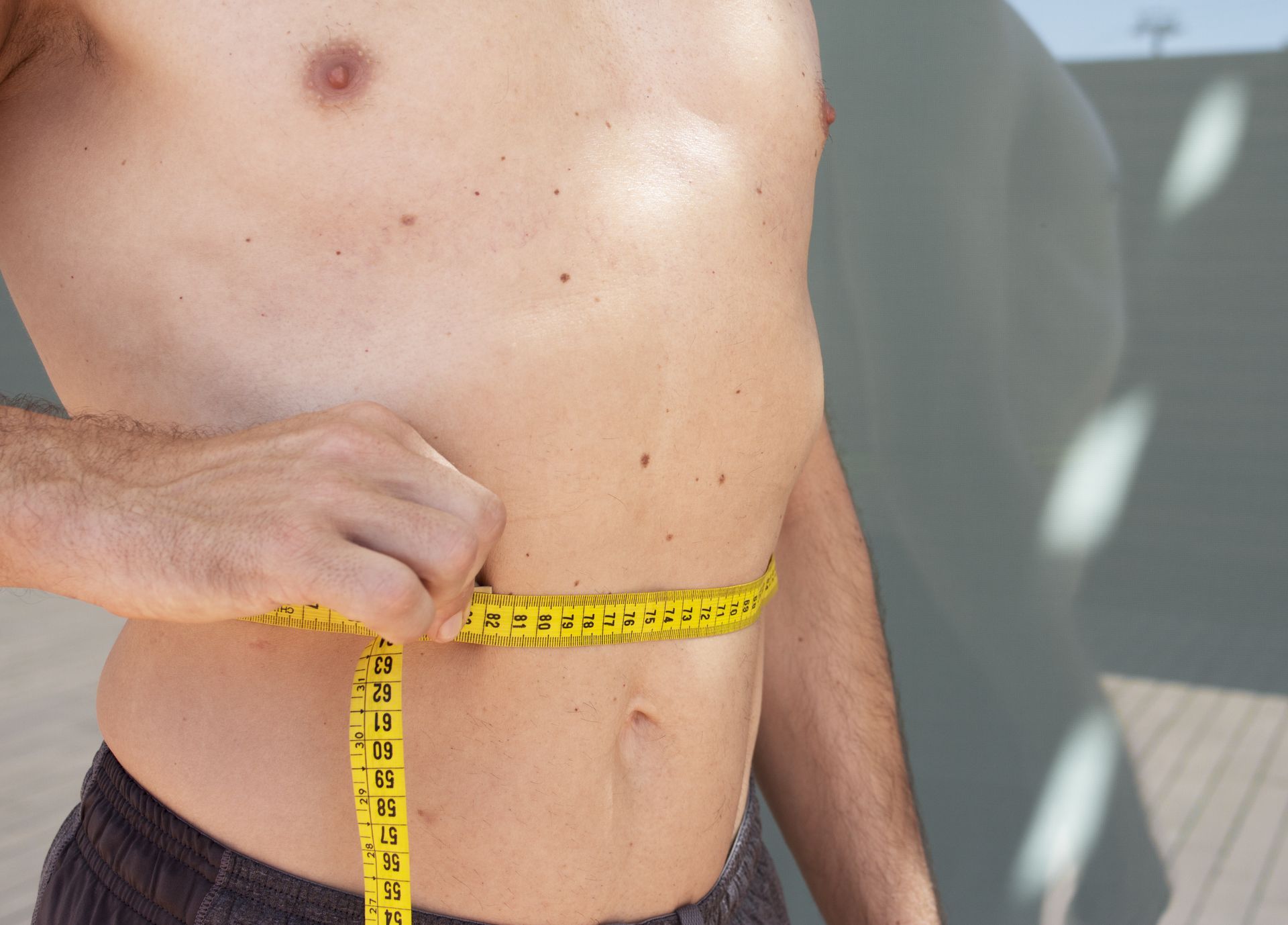 Person measuring waist with a yellow tape measure outdoors