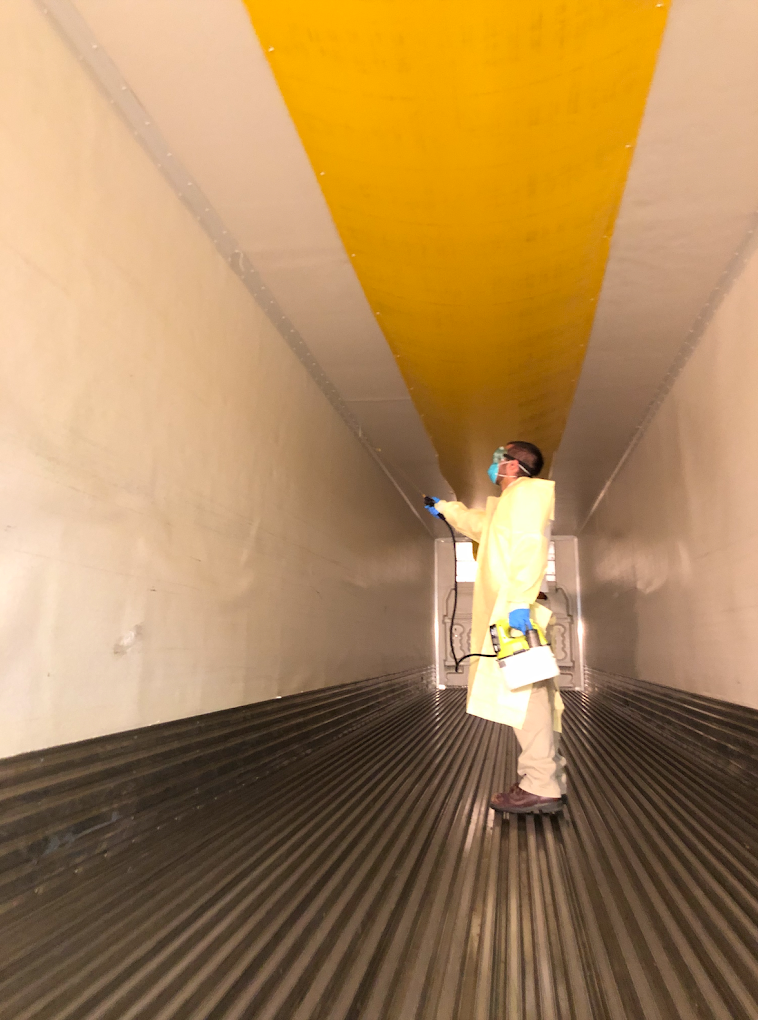 A man is standing in a long hallway with a yellow stripe on the ceiling.