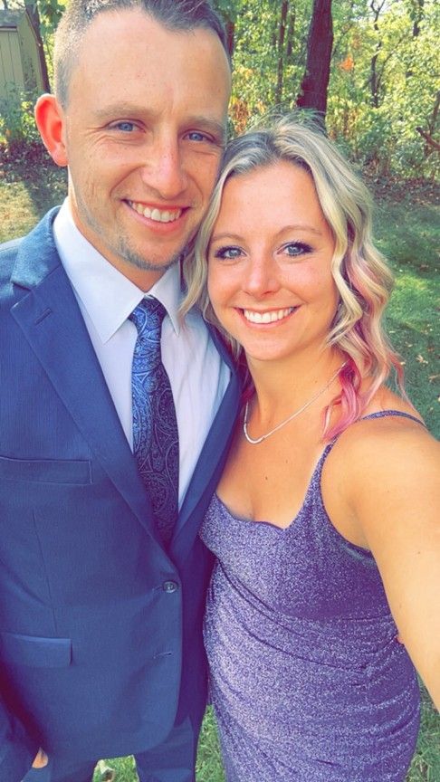 Smiling couple in formal attire posing outdoors among trees