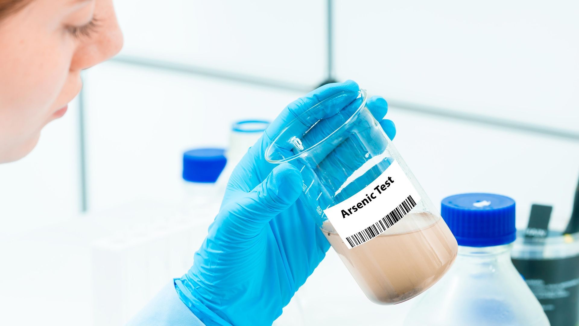 Gloved technician holding a labeled sample vial in a laboratory setting