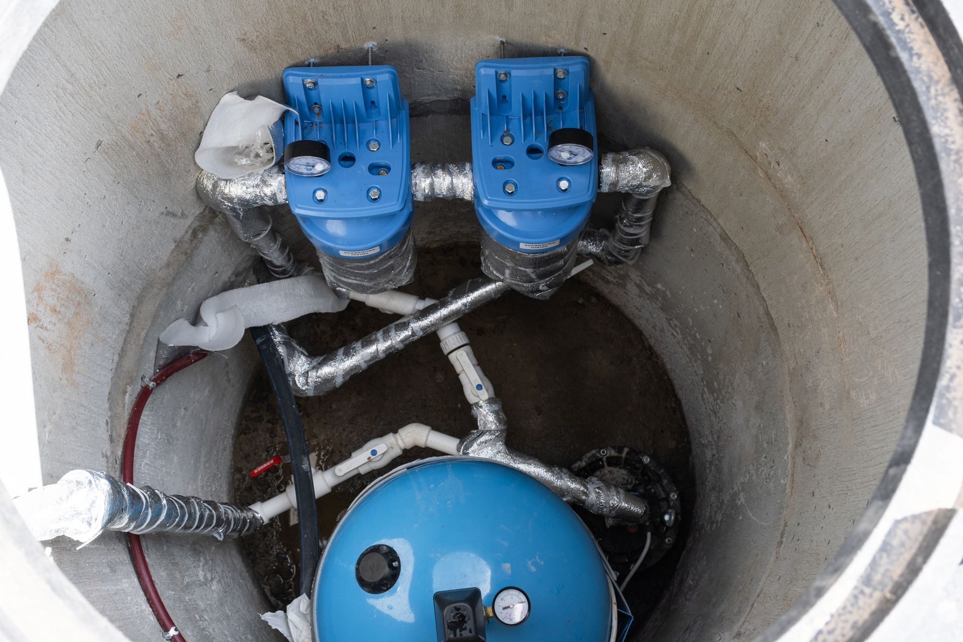 Blue valves and piping inside a concrete utility well with water at the bottom.