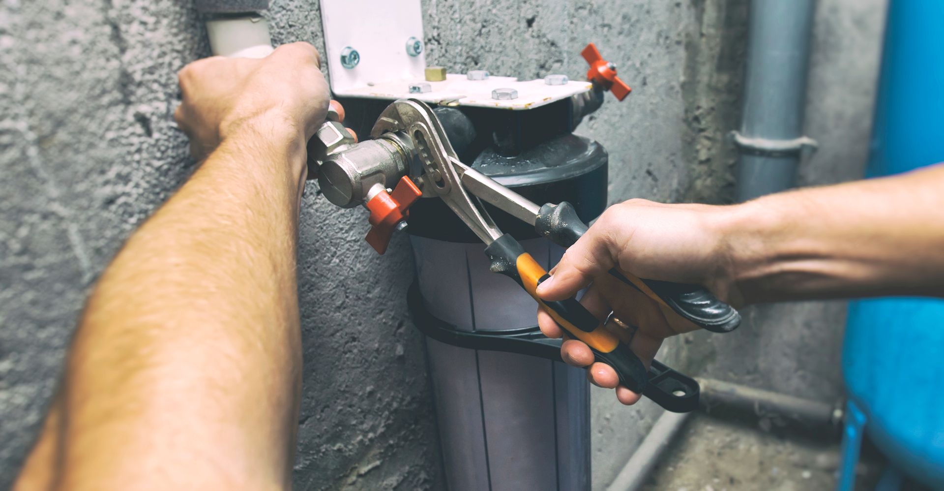 Two hands using pliers to work on a black pipe against a rough wall