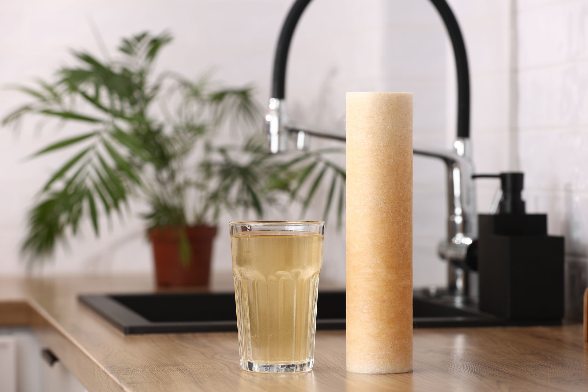Tall bamboo cup beside a glass on a kitchen counter near a sink and potted plant
