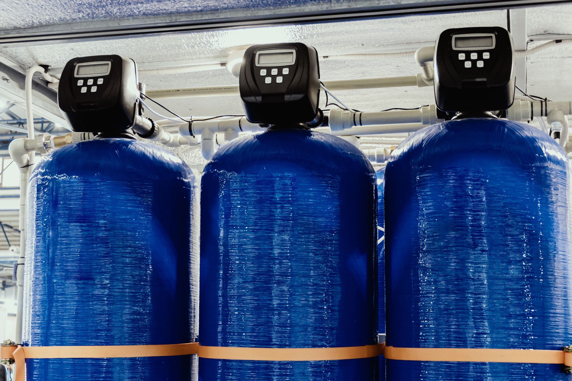 Three large blue industrial tanks with black control heads in a factory setting