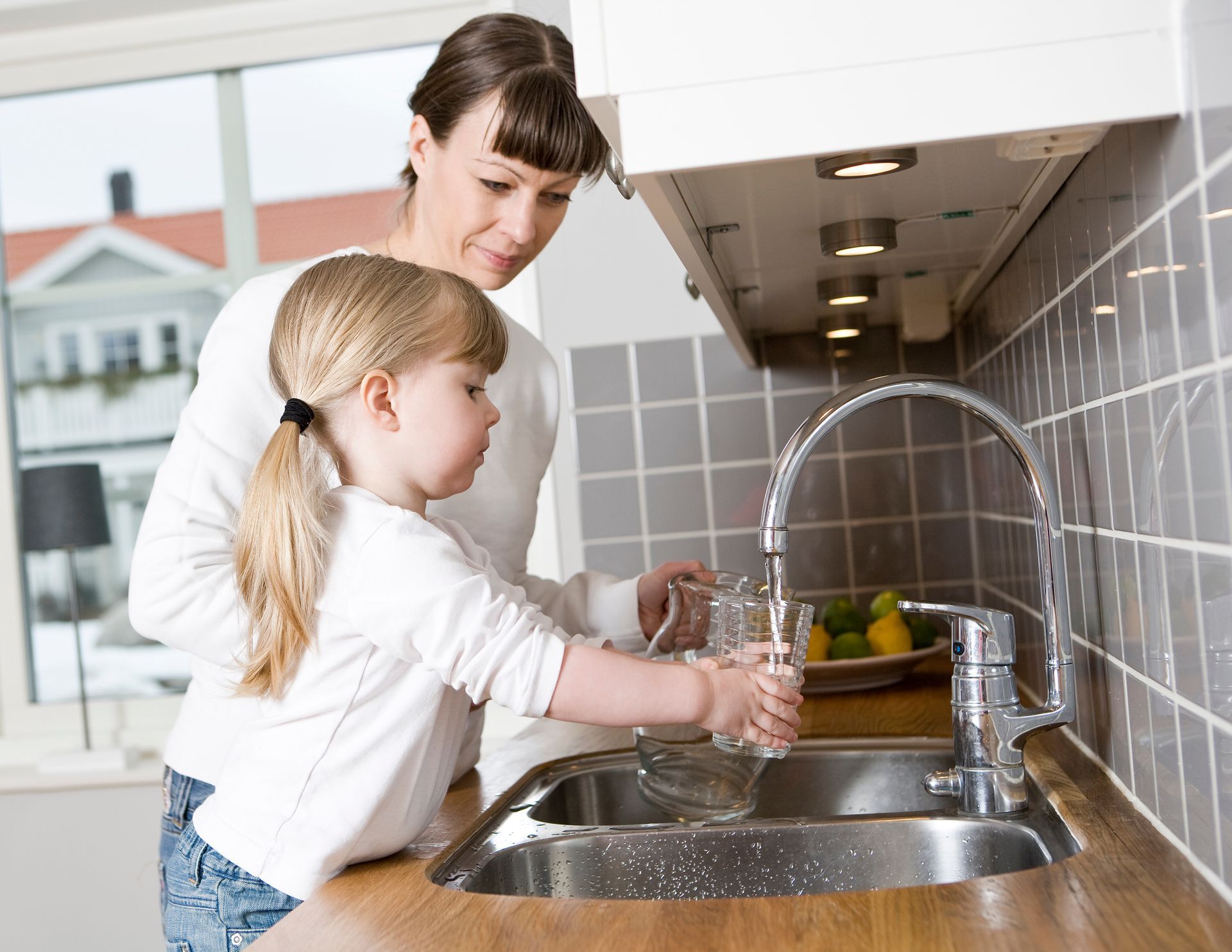 Hand washing a glass under a kitchen faucet with running water
