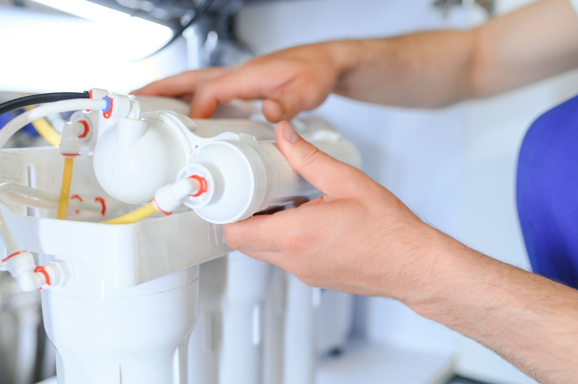 Hands assembling a white water filter system under a sink with exposed tubing and parts